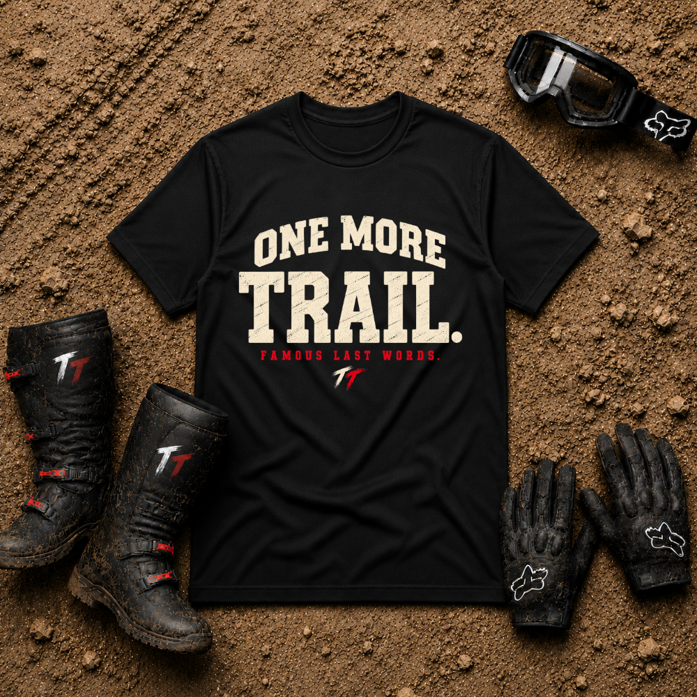 Black One More Trail t-shirt with vintage varsity print and 'Famous Last Words' tagline — flat lay with muddy boots, goggles, and gloves, Tire Time Offroad